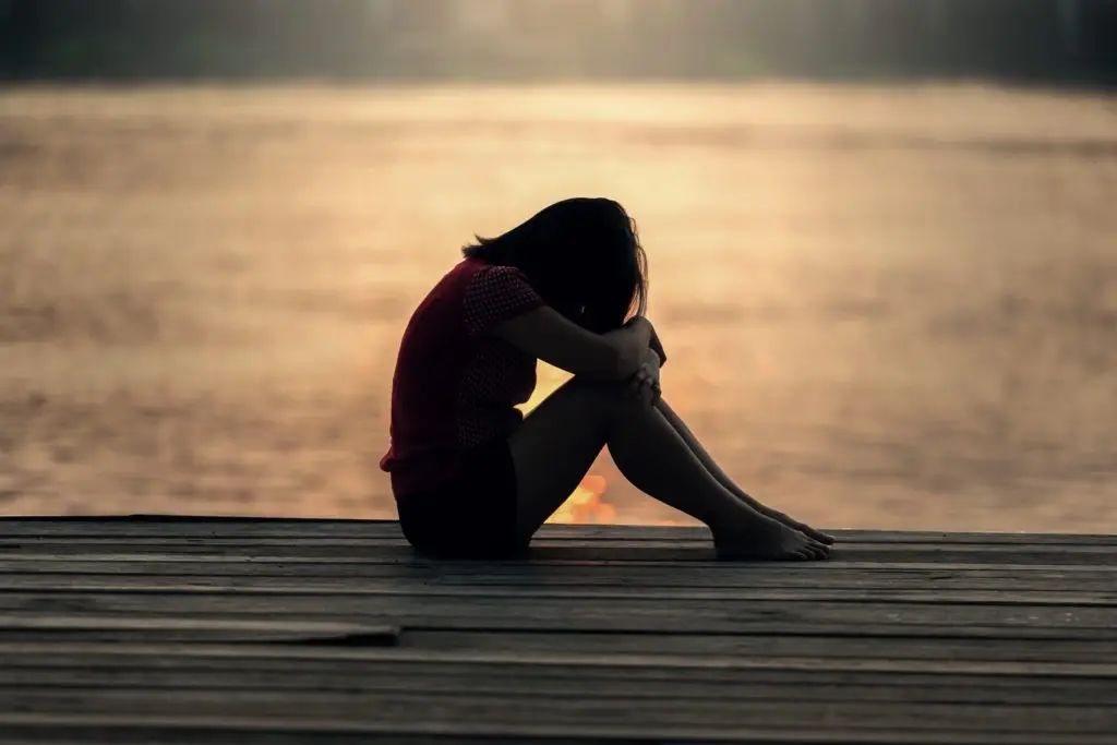 girl sitting with head in her lap on a dock