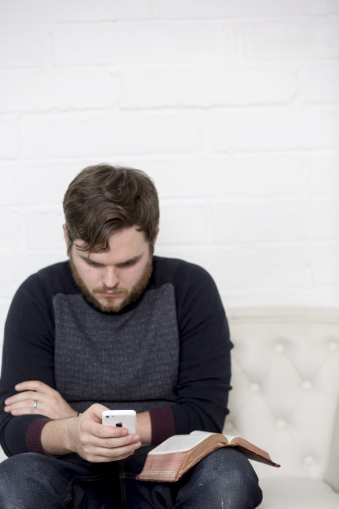 man looking at his phone with Bible on his knee