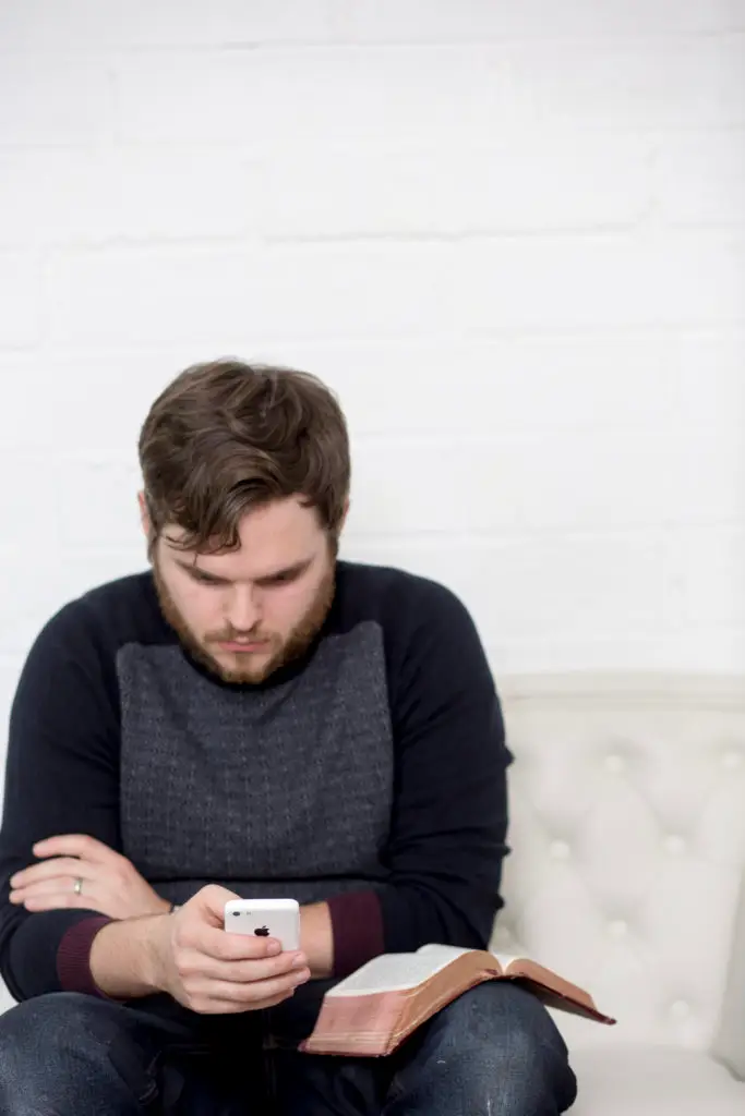 man looking at his phone with Bible on his knee