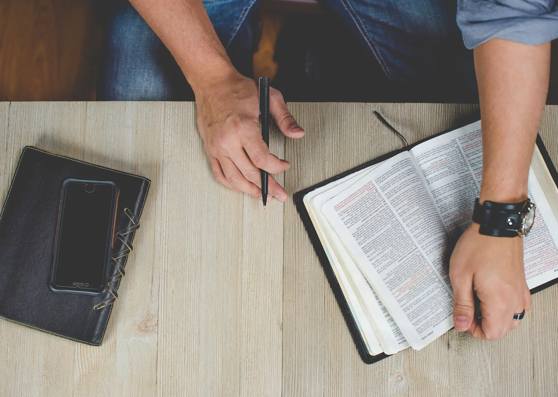 man's hand holding pen over Bible