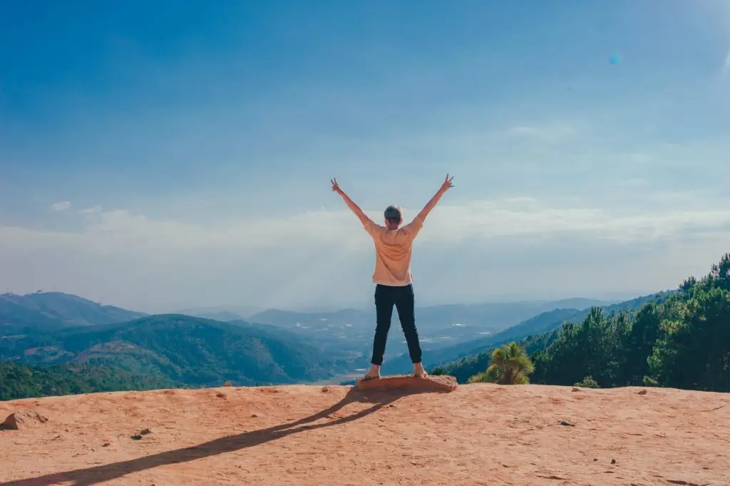 woman at the edge of a cliff with arms raised