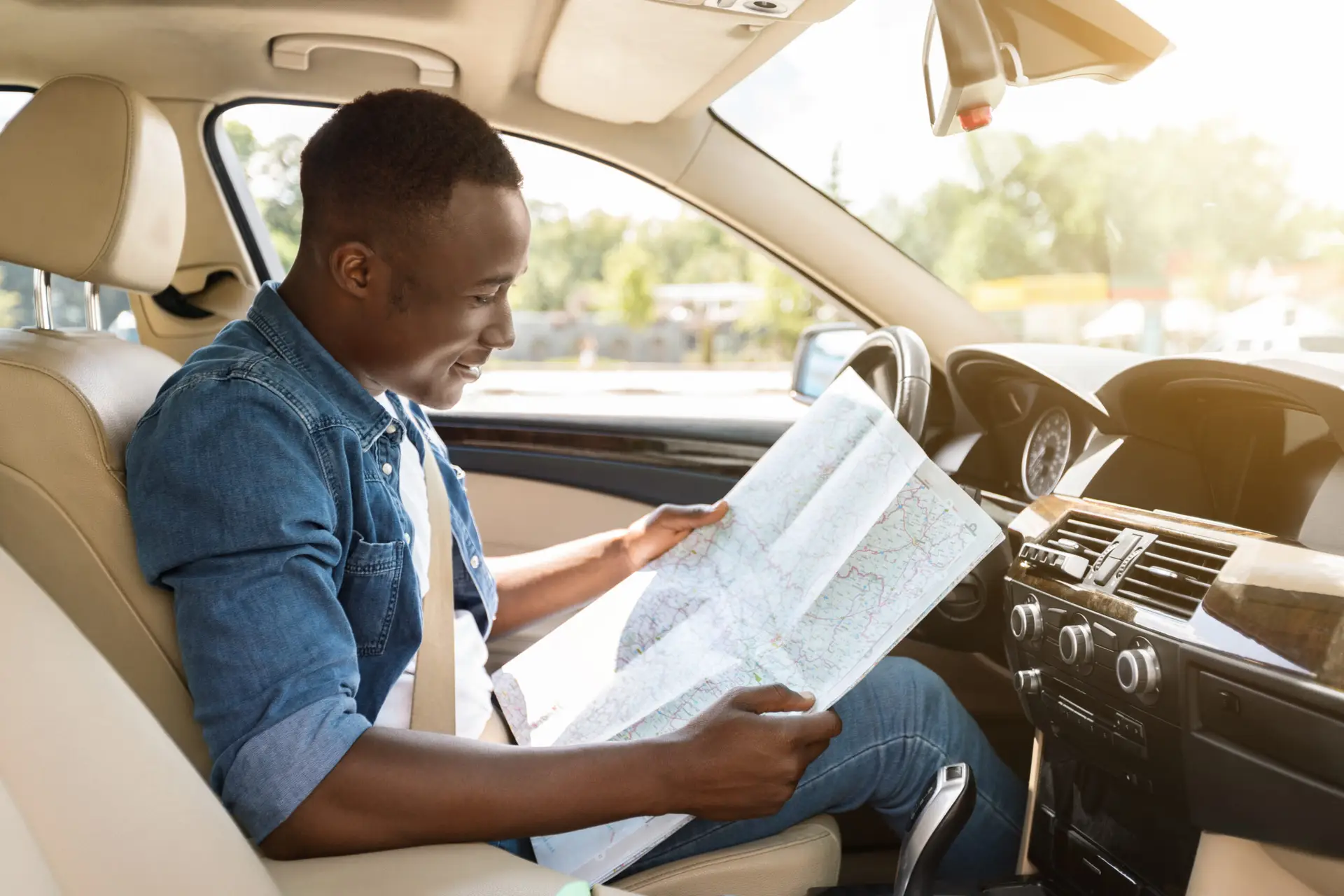 Smiling guy driver reading map while sitting in comfortable car