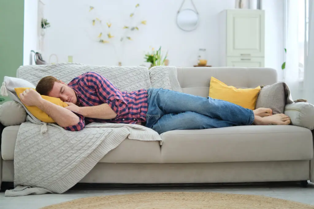 weary man in jeans and shirt succumbs to a nap on his couch