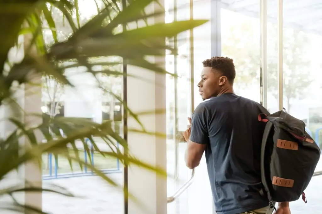 College student exits glass door with backpack on shoulder