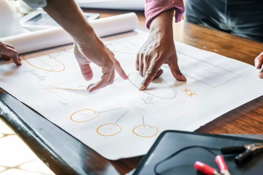 Hands pointing to parts of a strategic plan written out on a roll of white paper on a table.