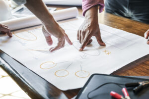 Hands pointing to parts of a strategic plan written out on a roll of white paper on a table.