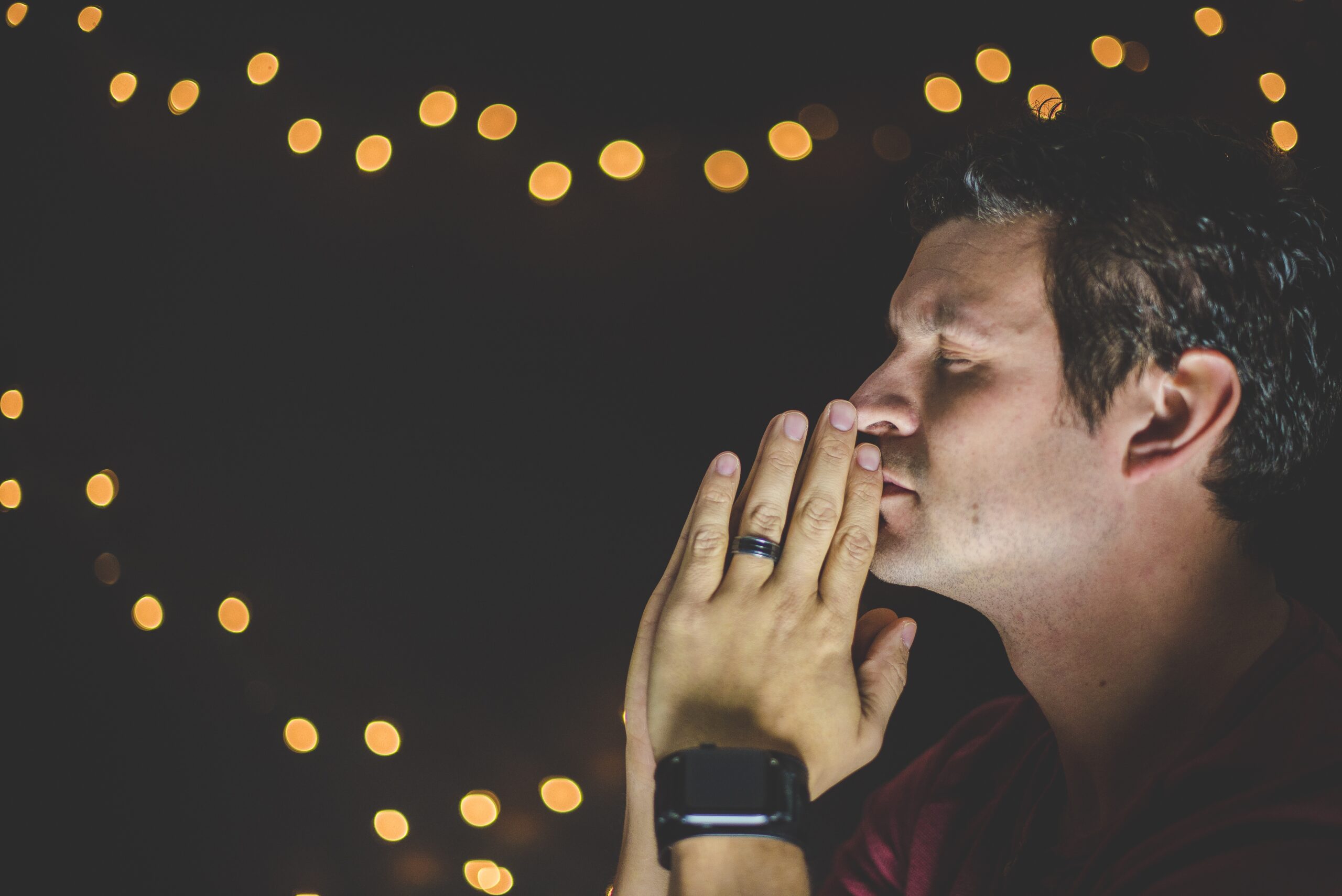 Closeup shot of a person praying with clenched hands and bokeh lights in the background