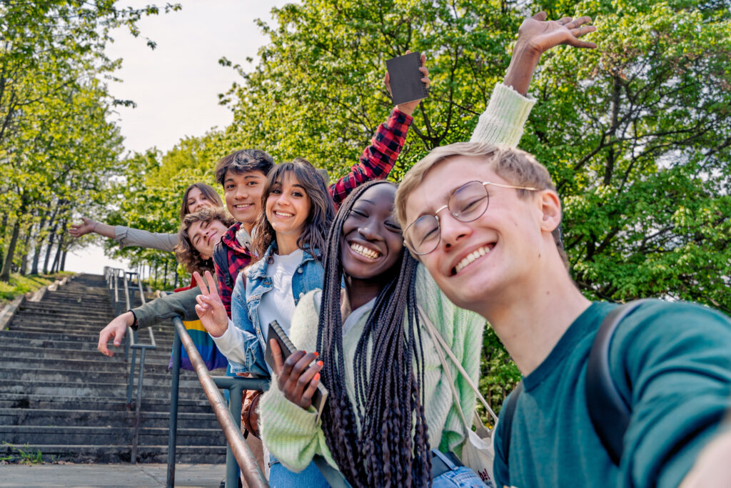 A diverse group of high school seniors taking a selfie outdoors, smiling and having fun