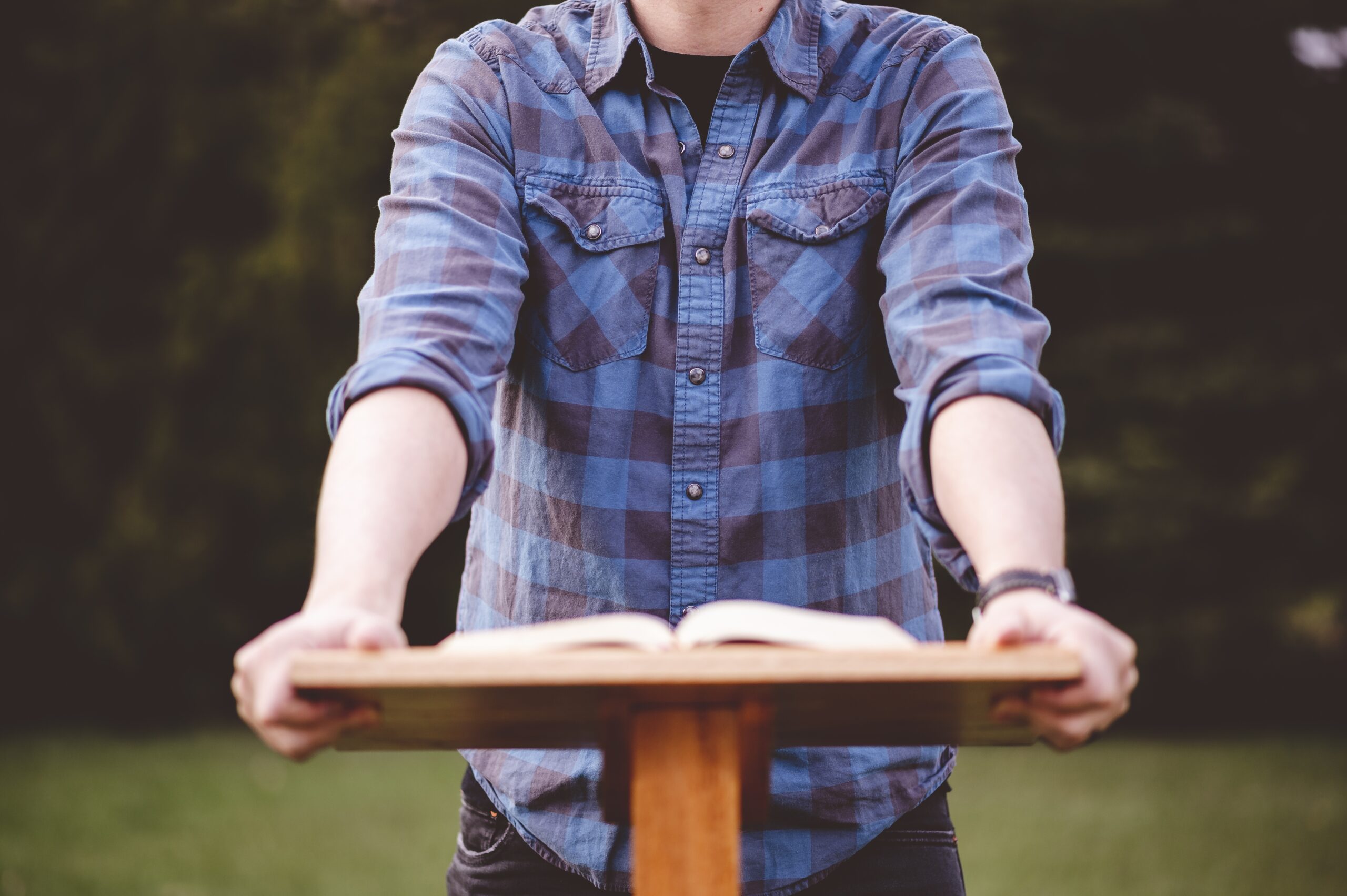 A man standing near a wooden stand with a Bible on it outside